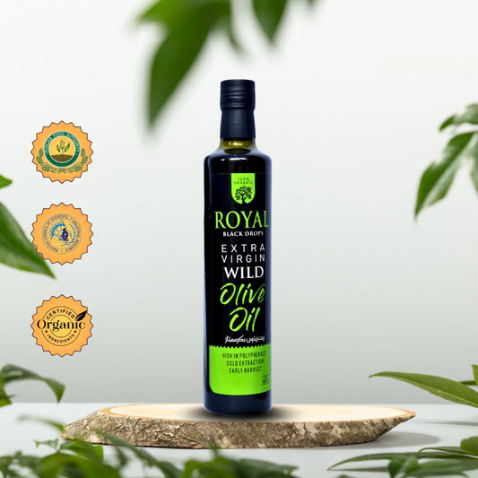 Bottle of Royal Black Drop Extra Virgin Wild Olive Oil on a wooden board with green leaves in the background